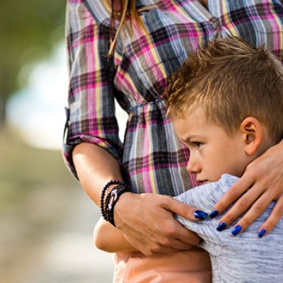 A small boy clings to his carer